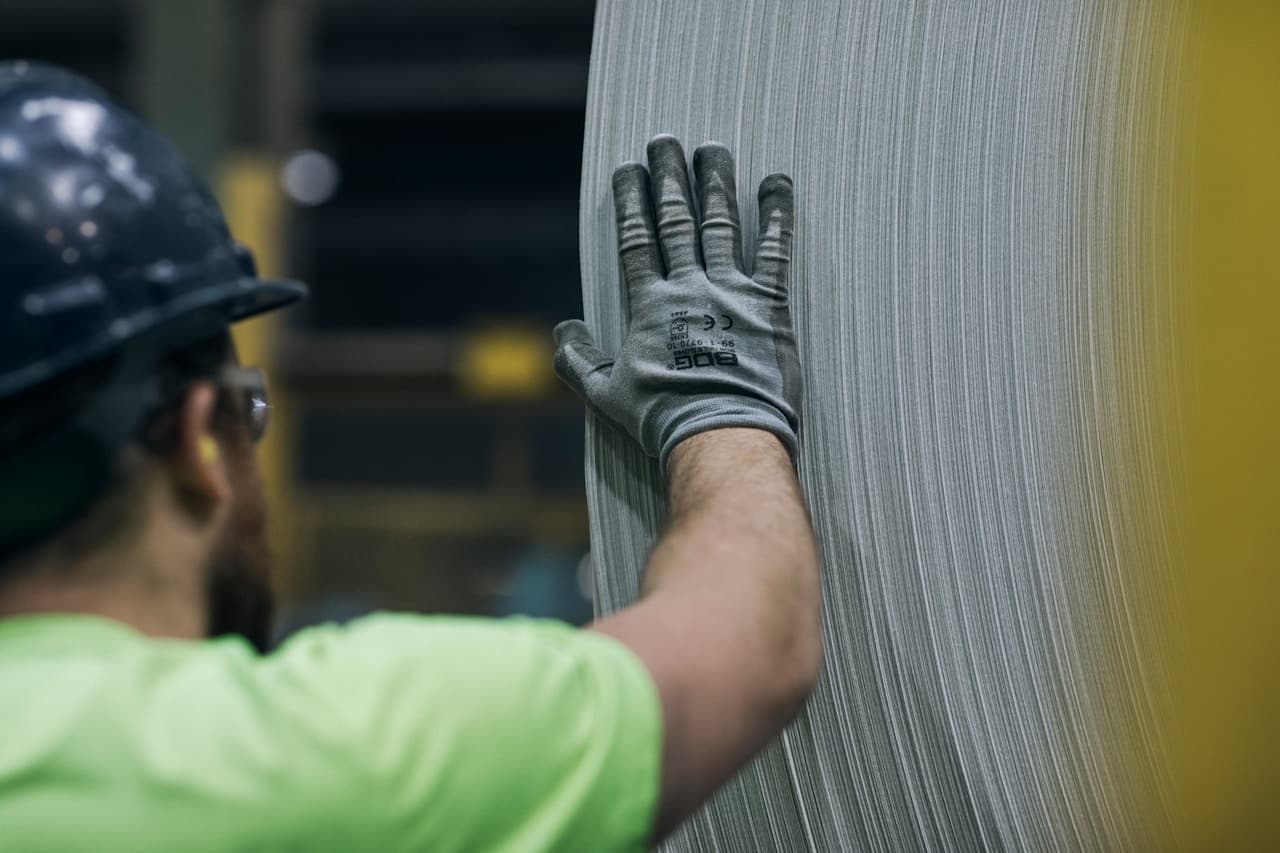 Trabalhador com capacete e EPI manuseando peça metálica em ambiente industrial
